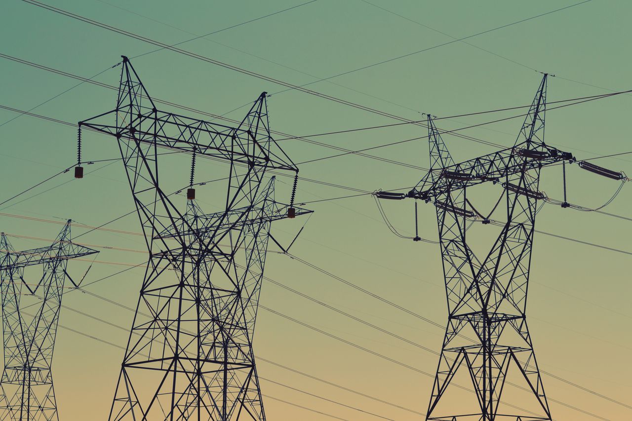 Silhouette of high voltage power lines against a twilight sky, illustrating energy infrastructure.
