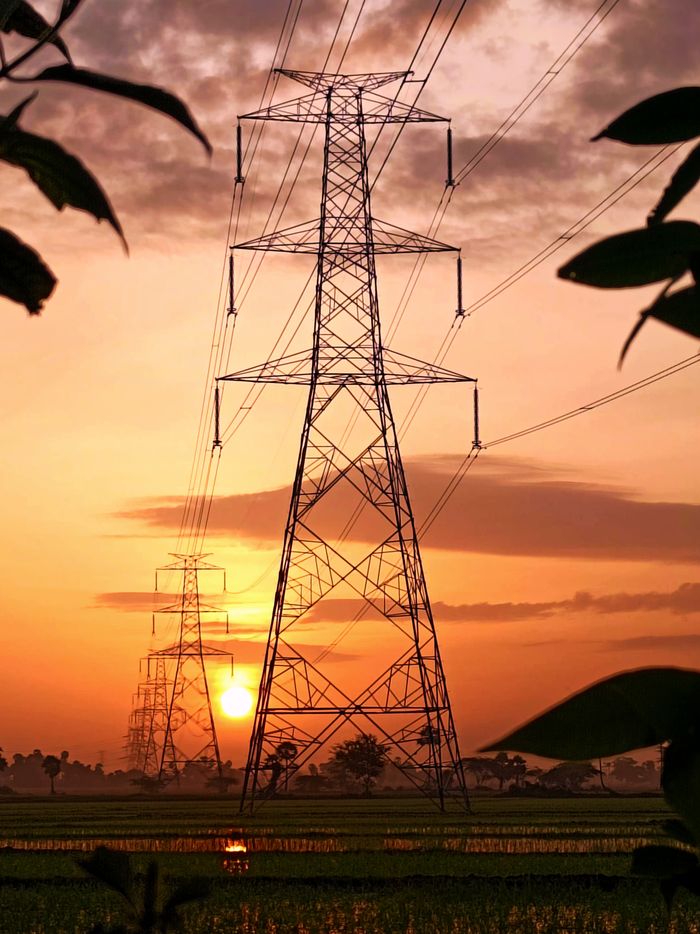 A dramatic sunset with silhouetted power transmission towers against a vibrant sky.