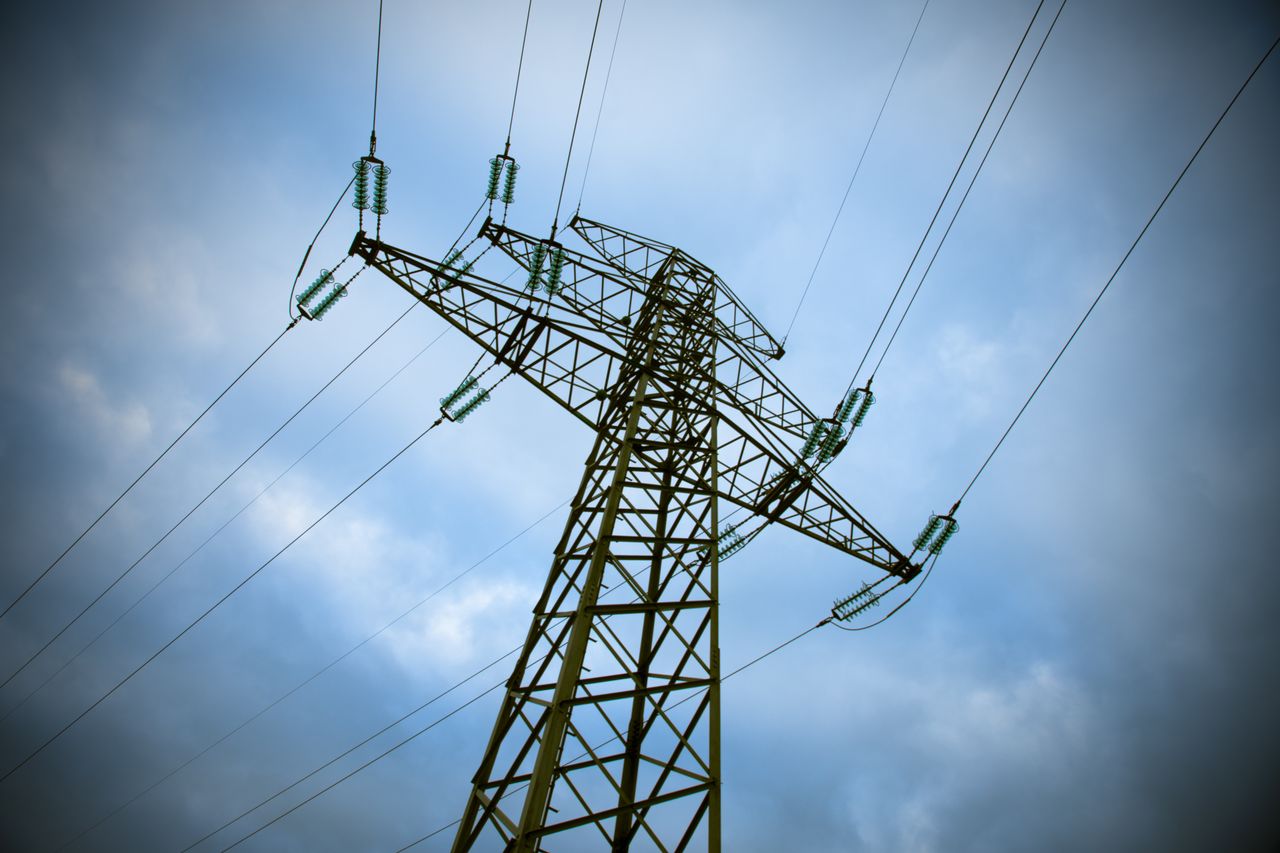 services-05 A majestic transmission tower stands tall against a cloudy blue sky, showcasing modern electric infrastructure.